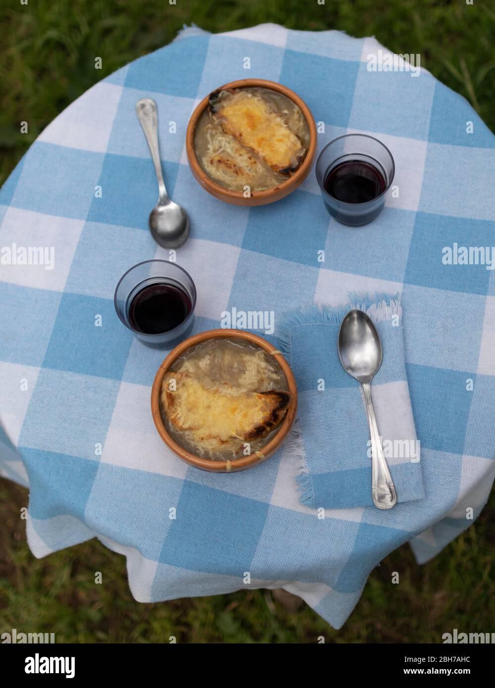 Traditional gratin onion soup dishes. Top view of a rustic table with blue squared tablecloth and ceramic plates with glasses of wine. Stock Photo