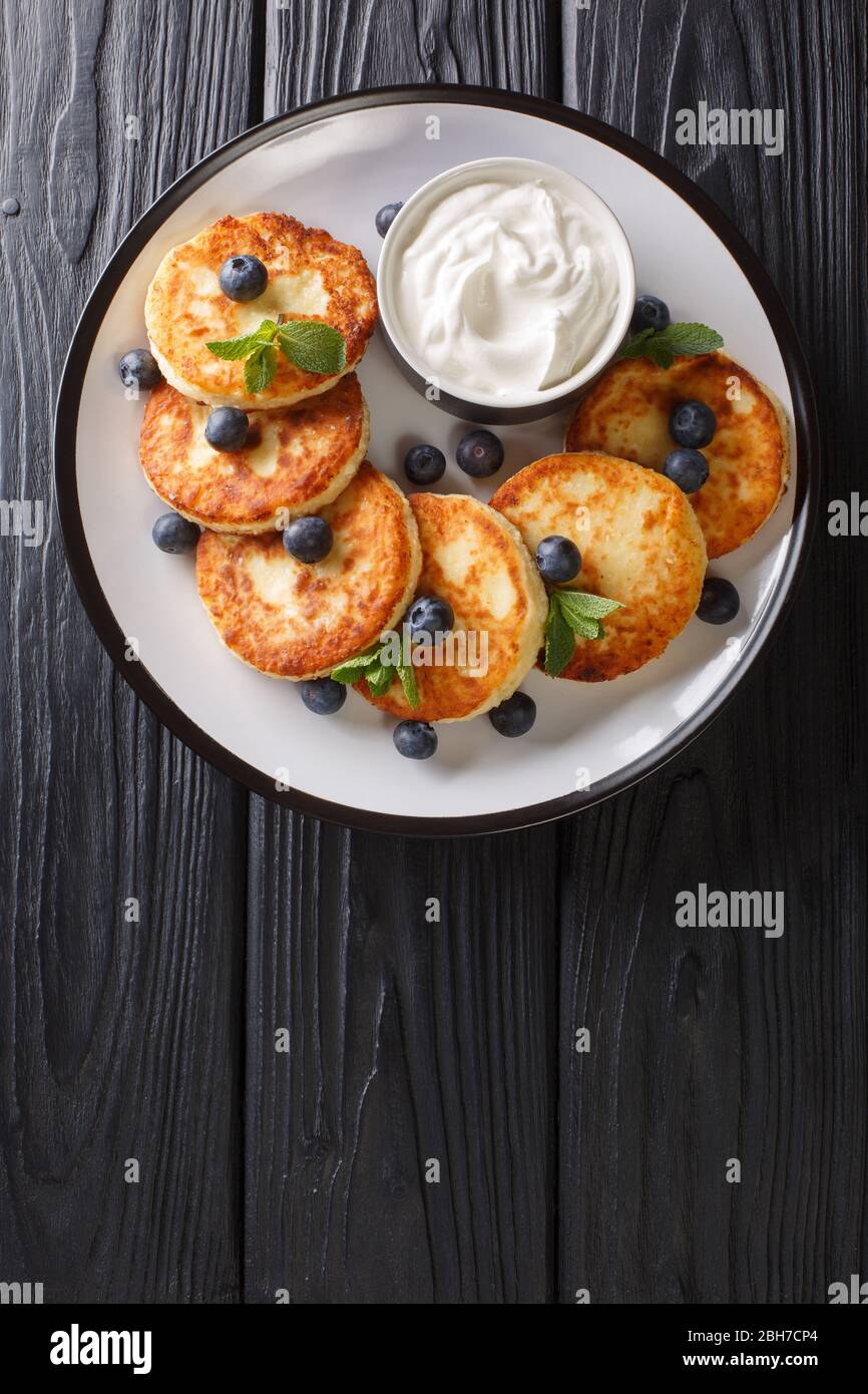 Healthy breakfast of cottage cheese syrniki with blueberries, mint and sour cream close-up in a plate on the table. vertical top view from above Stock Photo