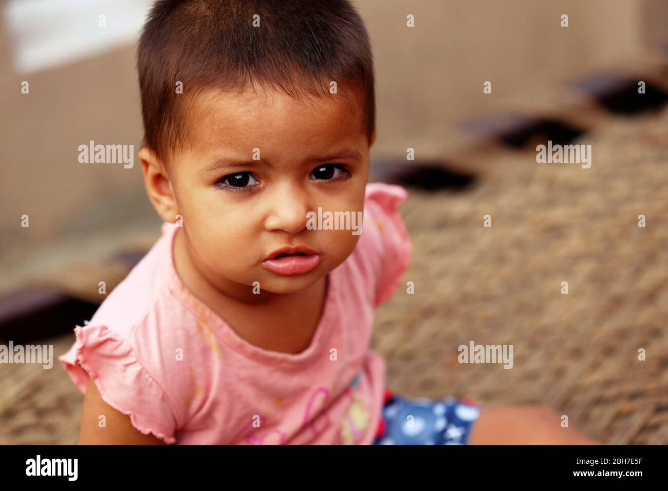 Close Up portrait of Cute innocent little girl sitting on cot and she looking at camera Stock Photo