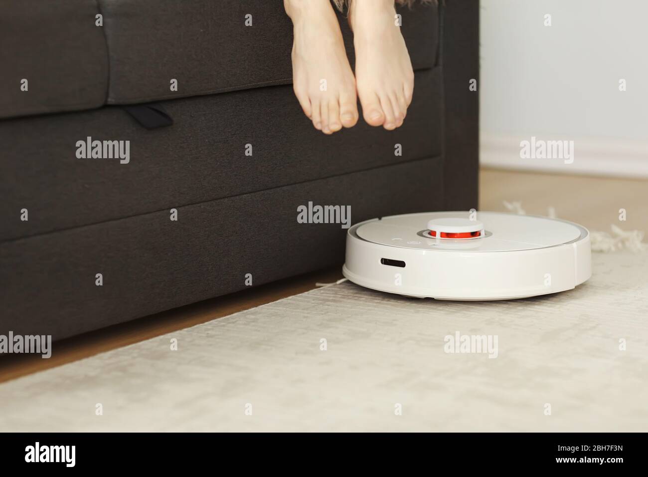 Robotic vacuum cleaner cleaning the room while woman resting on sofa