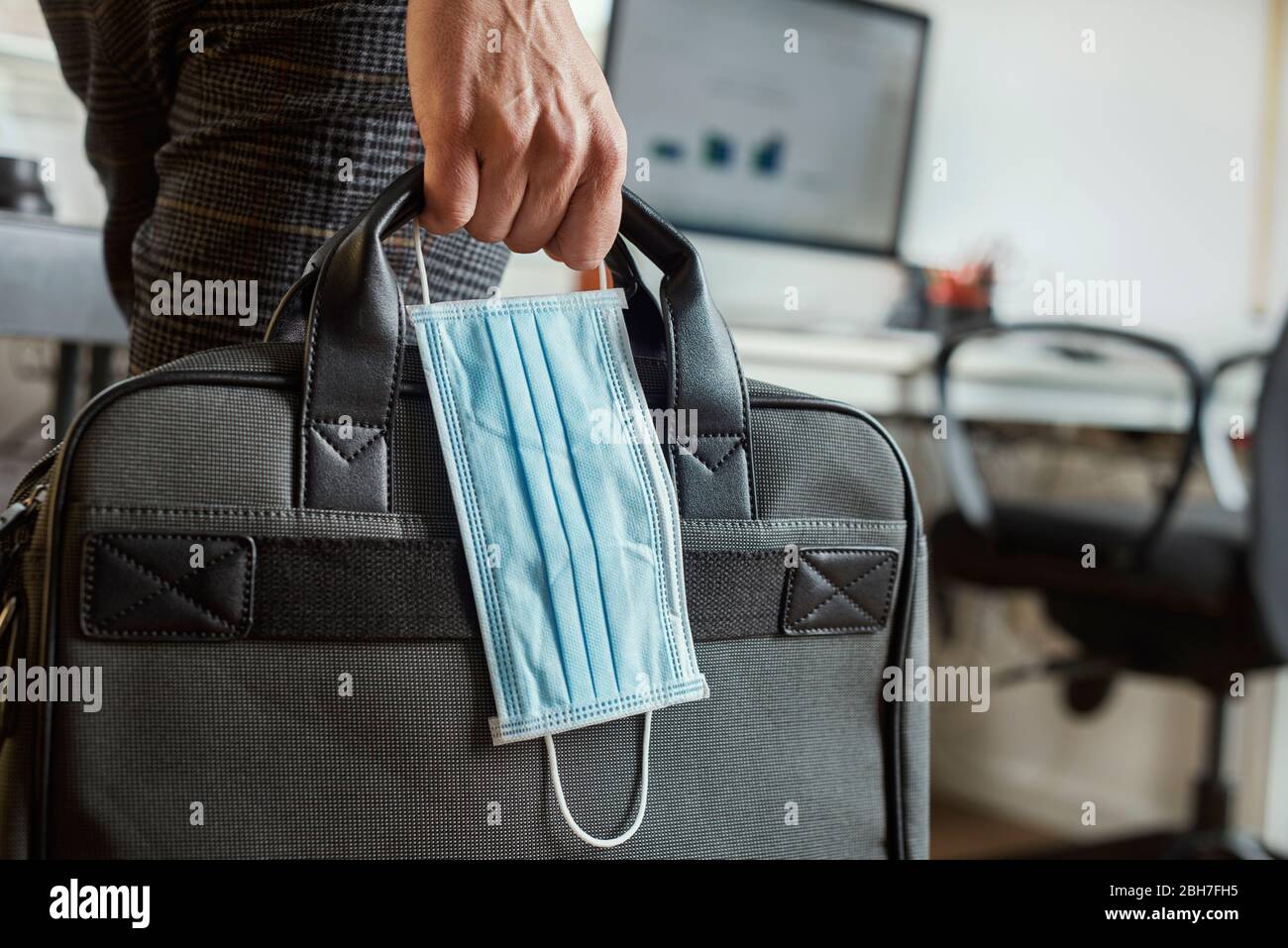 closeup of a young man in an office holding a briefcase and a surgical mask in his hand Stock Photo