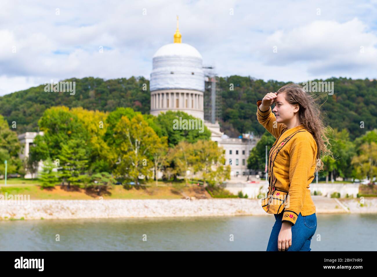 Charleston, West Virginia capital city with woman looking at scaffold construction on state capitol dome from university grounds by river Stock Photo