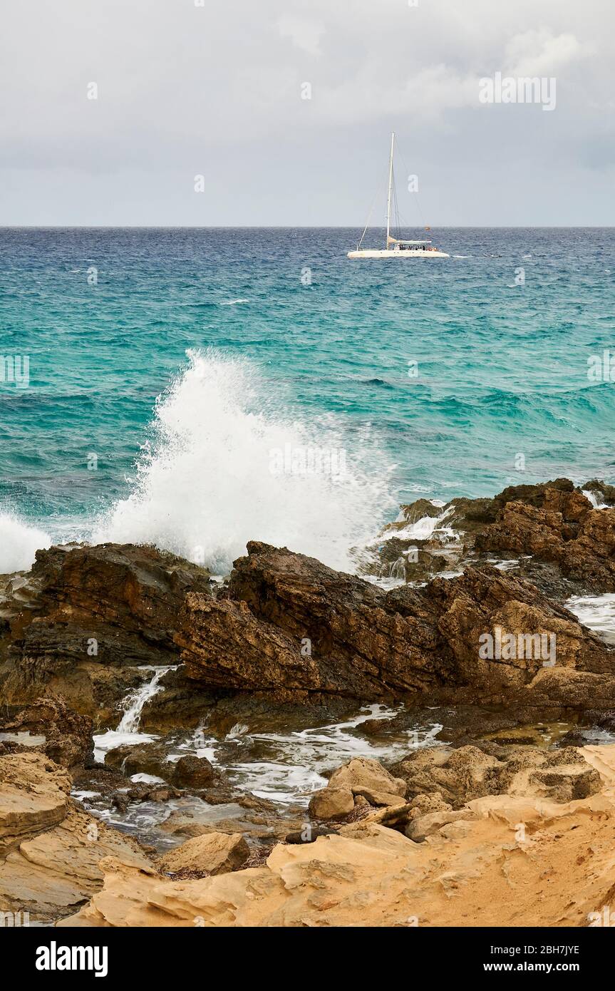 Sailing ship near Es Carnatge coastline with blue rough sea hiting rocks near Es Caló (Formentera, Pityuses, Balearic Islands,Mediterranean sea,Spain) Stock Photo