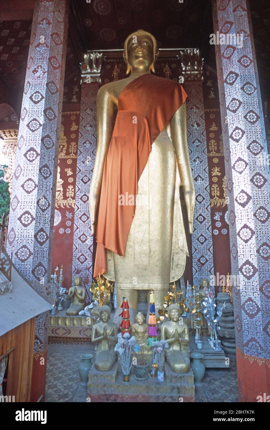 Gold statue of the Buddha, draped with an orange sash, in an elaborately decorated temple or wat in Luang Prabang, Laos, SE Asia. The town of Luang Prabang is a UNESCO World Heritage Site. Stock Photo
