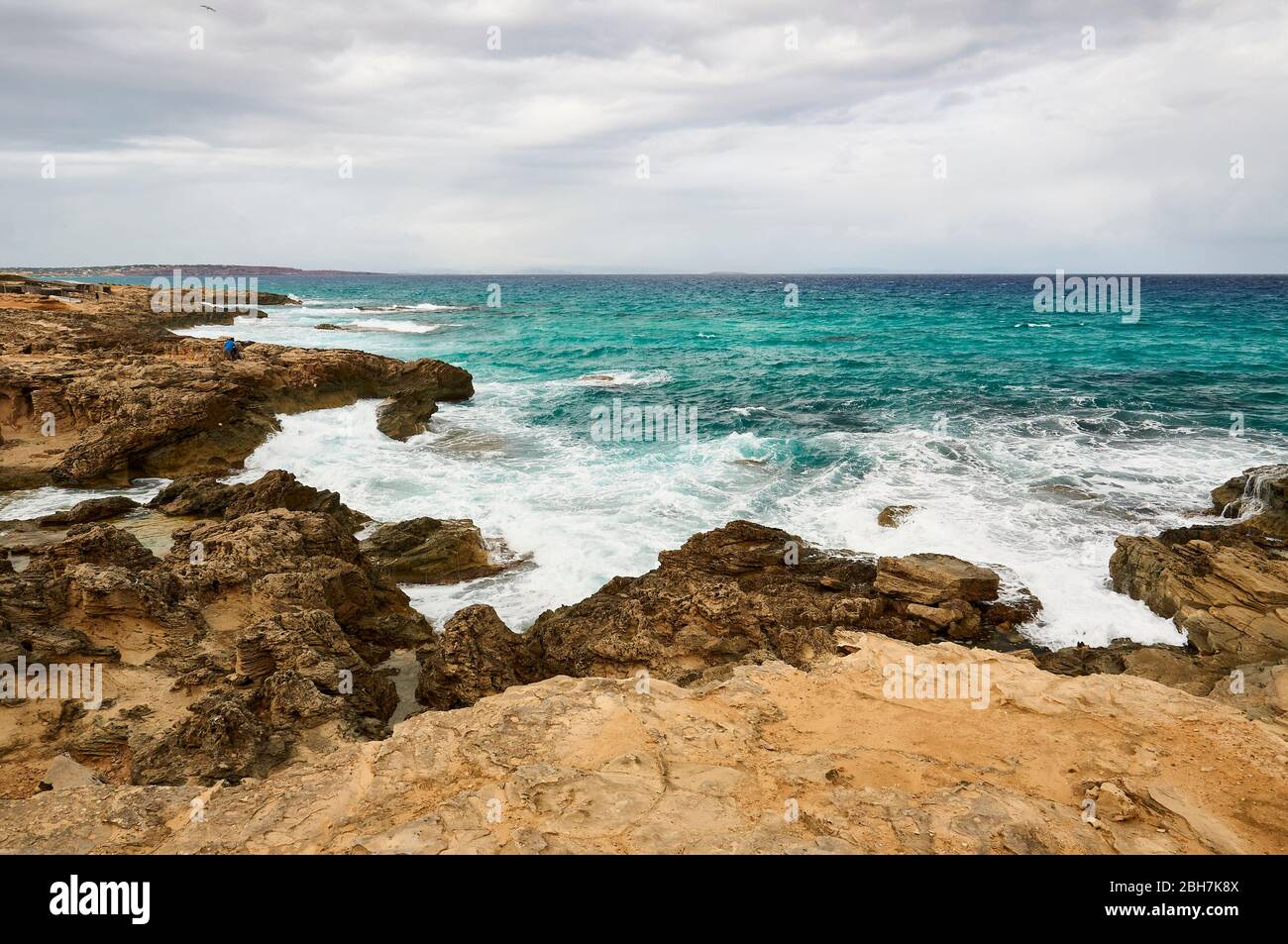 Fisherman on the rocks by Es Carnatge coastline with blue rough waters near Es Caló (Formentera, Pityuses, Balearic Islands, Mediterranean sea, Spain) Stock Photo