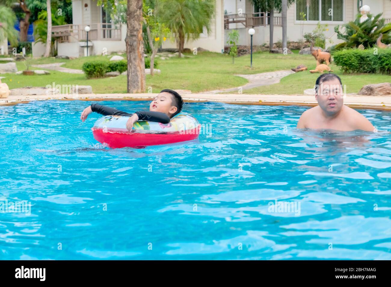 The fat boy in blue swimming suite and red float playing happily in the