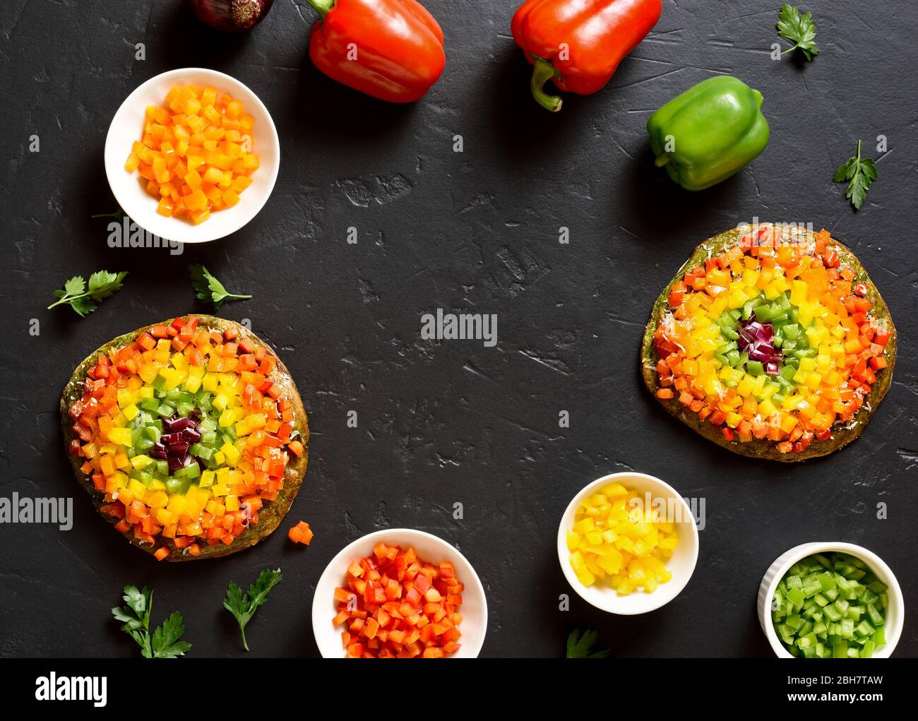 Frame of rainbow veggie bell peppers pizza and ingredients on black stone background. Vegetarian vegan or healthy food concept. Gluten free diet dish. Stock Photo