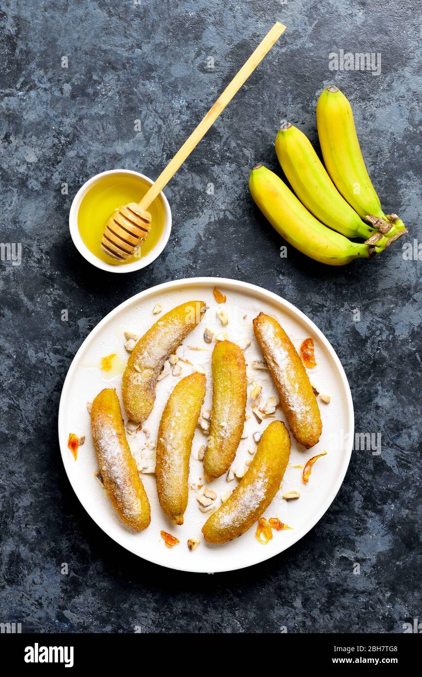 Deep fried bananas on white plate over blue stone background. Tasty