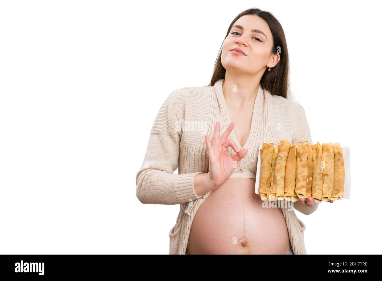 Proud pregnant woman making perfect gesture and holding pancakes isolated on white studio background Stock Photo