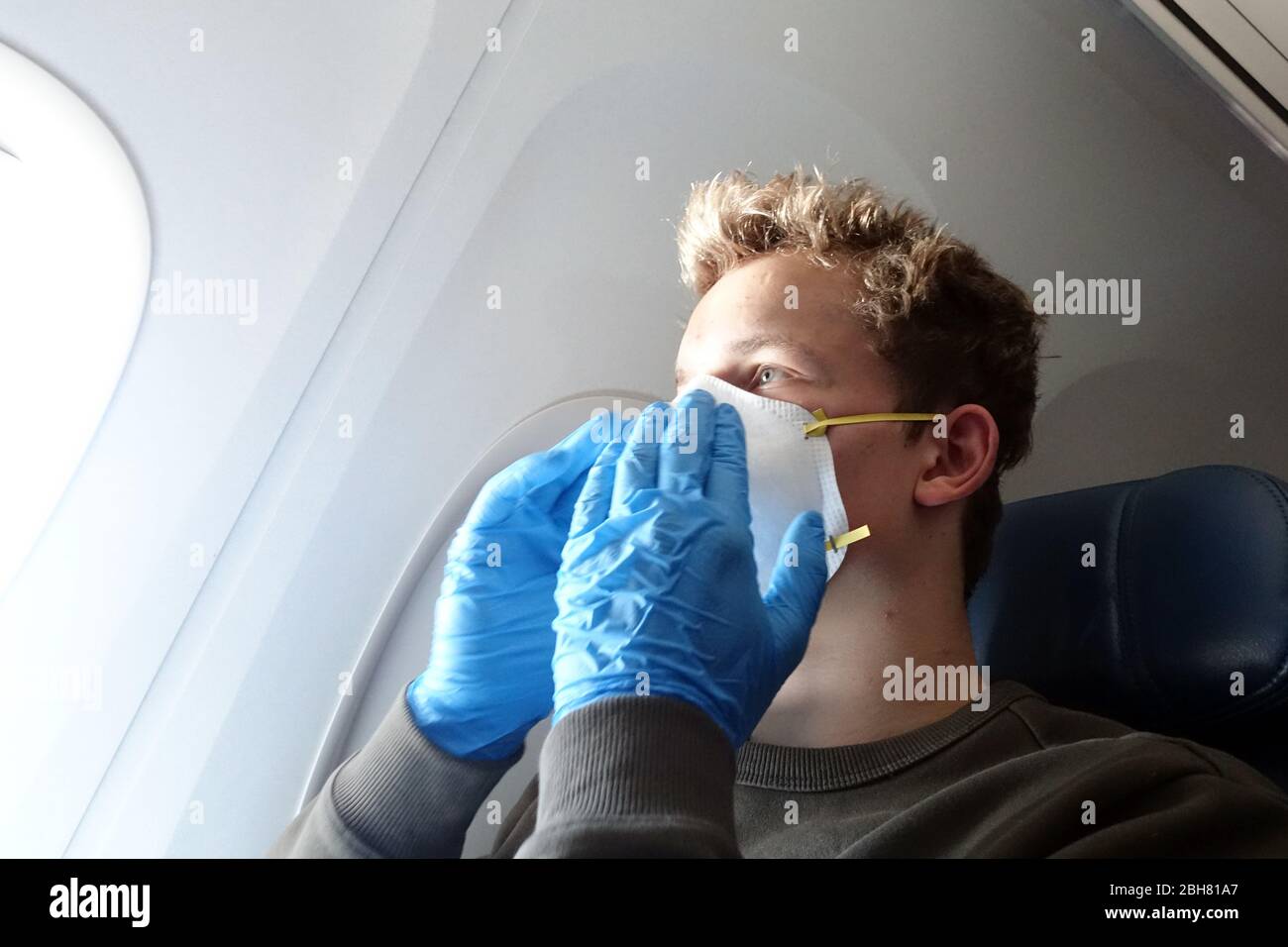 09.04.2020, Minneapolis, Minnesota, USA - Teenager in times of corona pandemic sitting in an airplane with a breathing mask and protective gloves. 00S Stock Photo