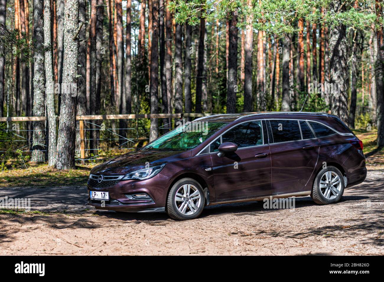Galkalne, Latvia - April 22, 2020: brown shiny car Opel Astra Sport Tourer  parked in forest roadside on blurred bokeh background on bright sunny day, Stock Photo
