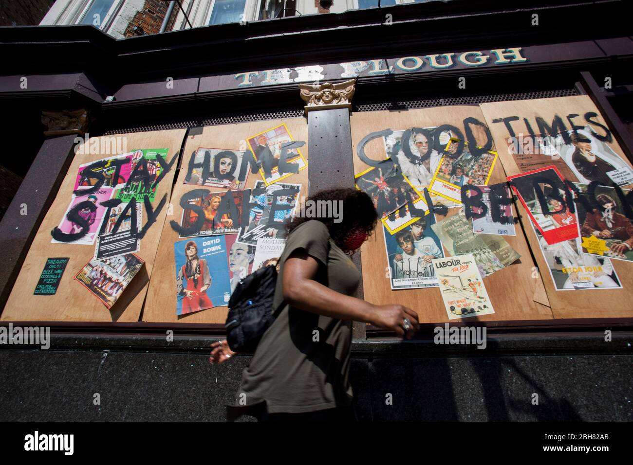 Homerton, London, UK. 24th Apr 2020. A woman wearing a face mask passes the boarded up Homerton pub in East London, calling people to stay home. Due to the Covid-19 outbreak. Credit: Marcin Nowak/Alamy Live News Stock Photo