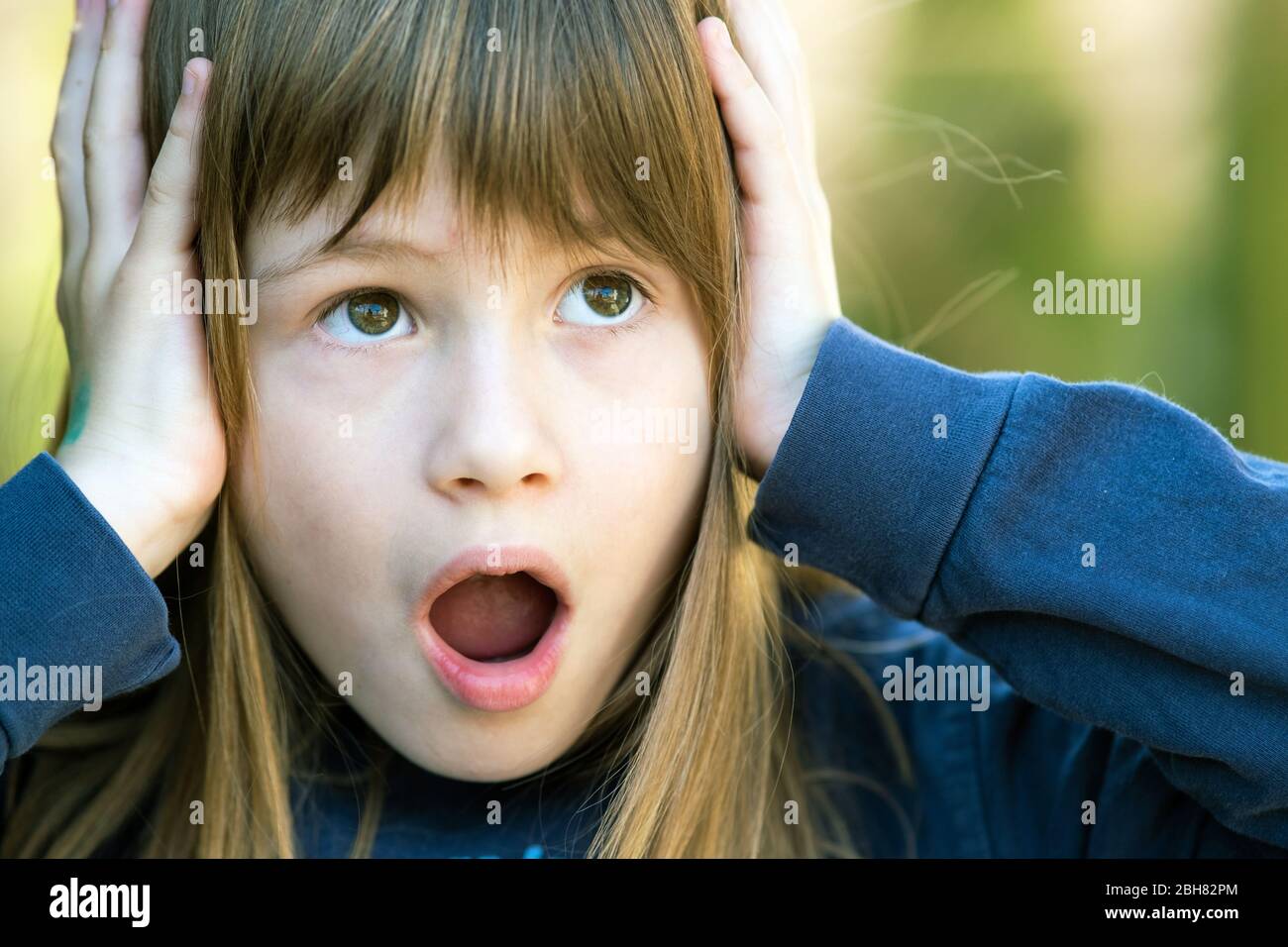 Portrait of surprised child girl holding hands to her head outdoors in ...