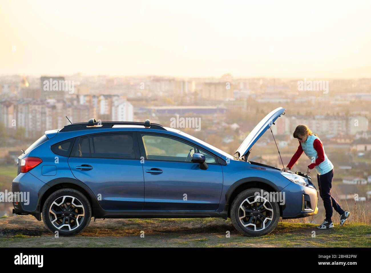 Young woman standing near broken down car with popped up hood having ...