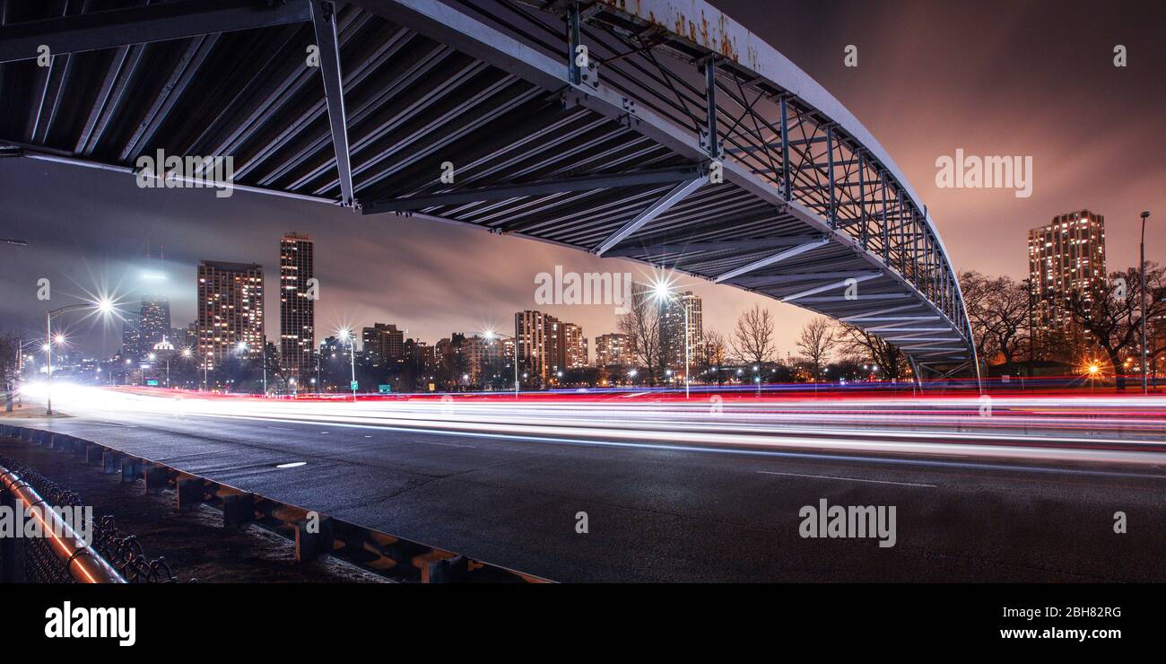 Long Exposure of the speed of traffic light trails at night under a steel bridge in the city Stock Photo