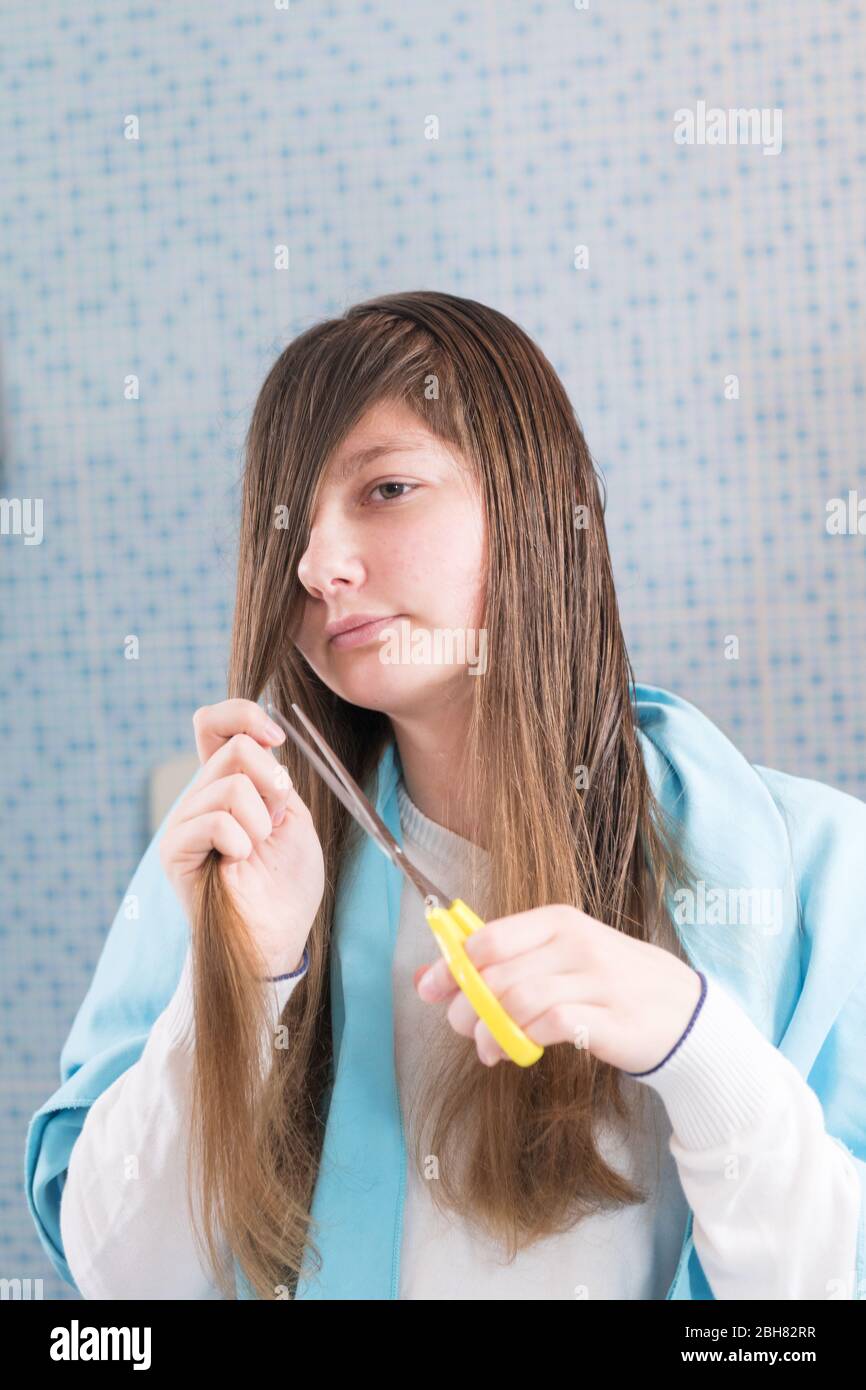 A girl is holding a scissor to cut her hair herself during lockdown of  coronavirus, looking in mirror making a shocked and funny face. DIY hair cut  du Stock Photo - Alamy