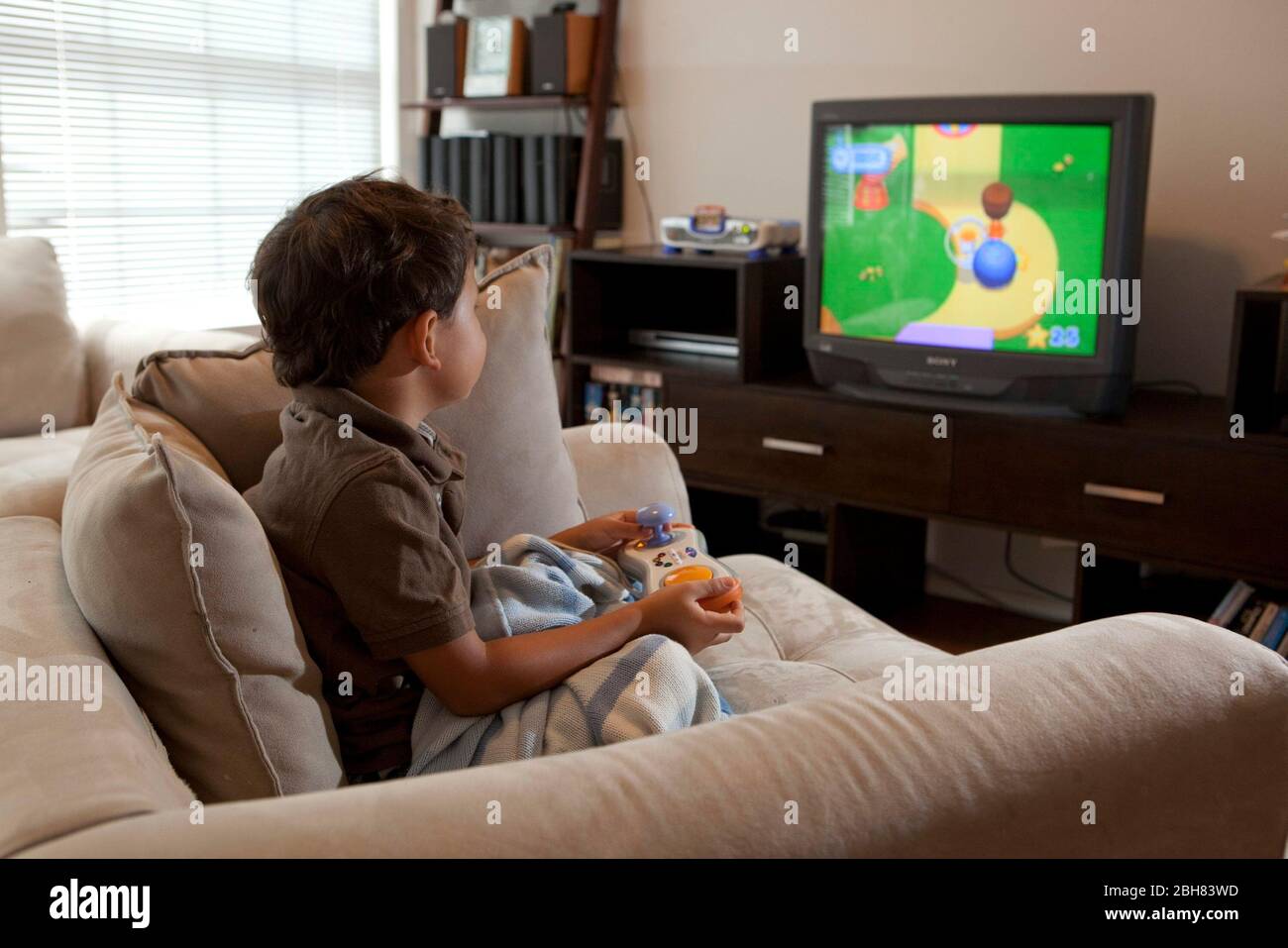 Austin, Texas  August 22, 2009:  Five-year old Mexican-American boy eating playing a video game while sitting in an over-stuffed chair at home on a Saturday morning. MR ©Bob Daemmrich Stock Photo