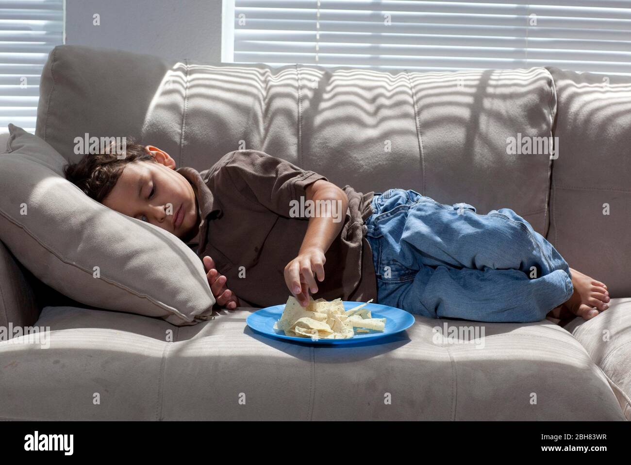 Austin, Texas  August 22, 2009:  Five-year old Mexican-American boy eating corn tortilla chips while sitting on an overstuffed couch at home on a Saturday morning.  MR   ©Bob Daemmrich Stock Photo