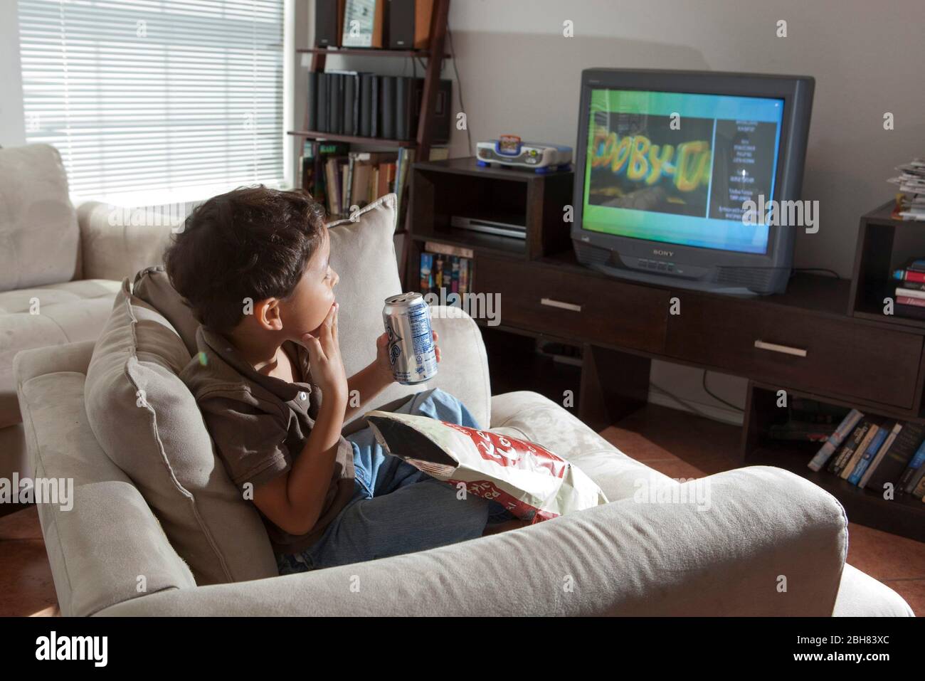 Austin, Texas  August 22, 2009: Five-year-old Mexican-American boy eating potato chips, drinking a soft drink and watching the Cartoon Network while sitting in an over-stuffed chair at home on a Saturday morning.  MR ©Bob Daemmrich Stock Photo