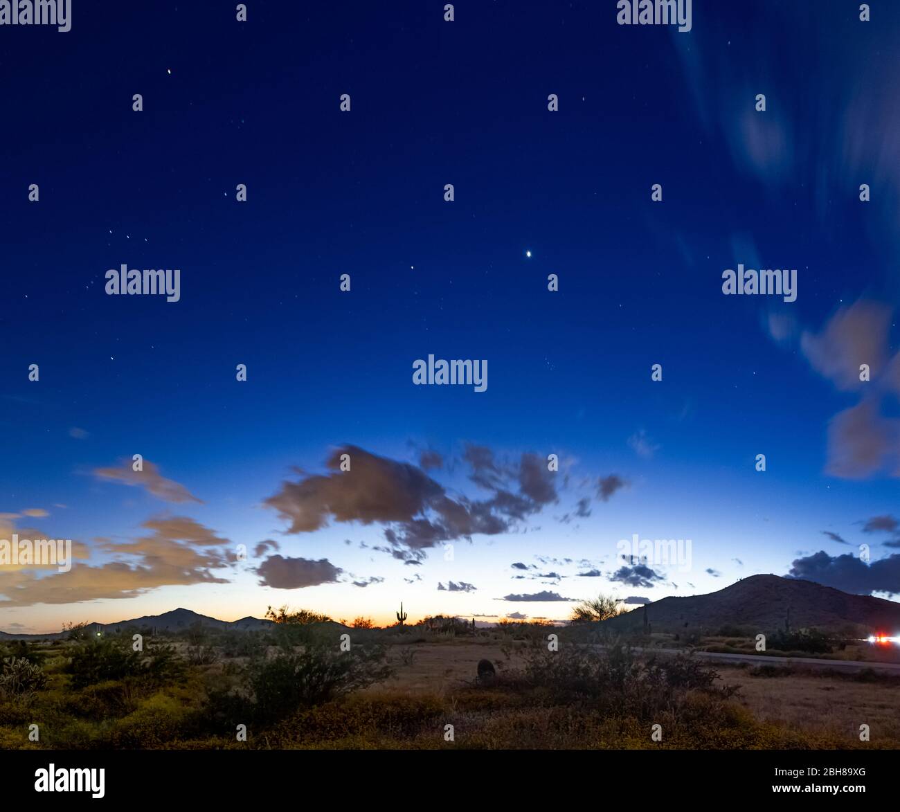 Evening image of the desert night sky during the blue hour with dramatic clouds and stars with a mountain landscape. Stock Photo