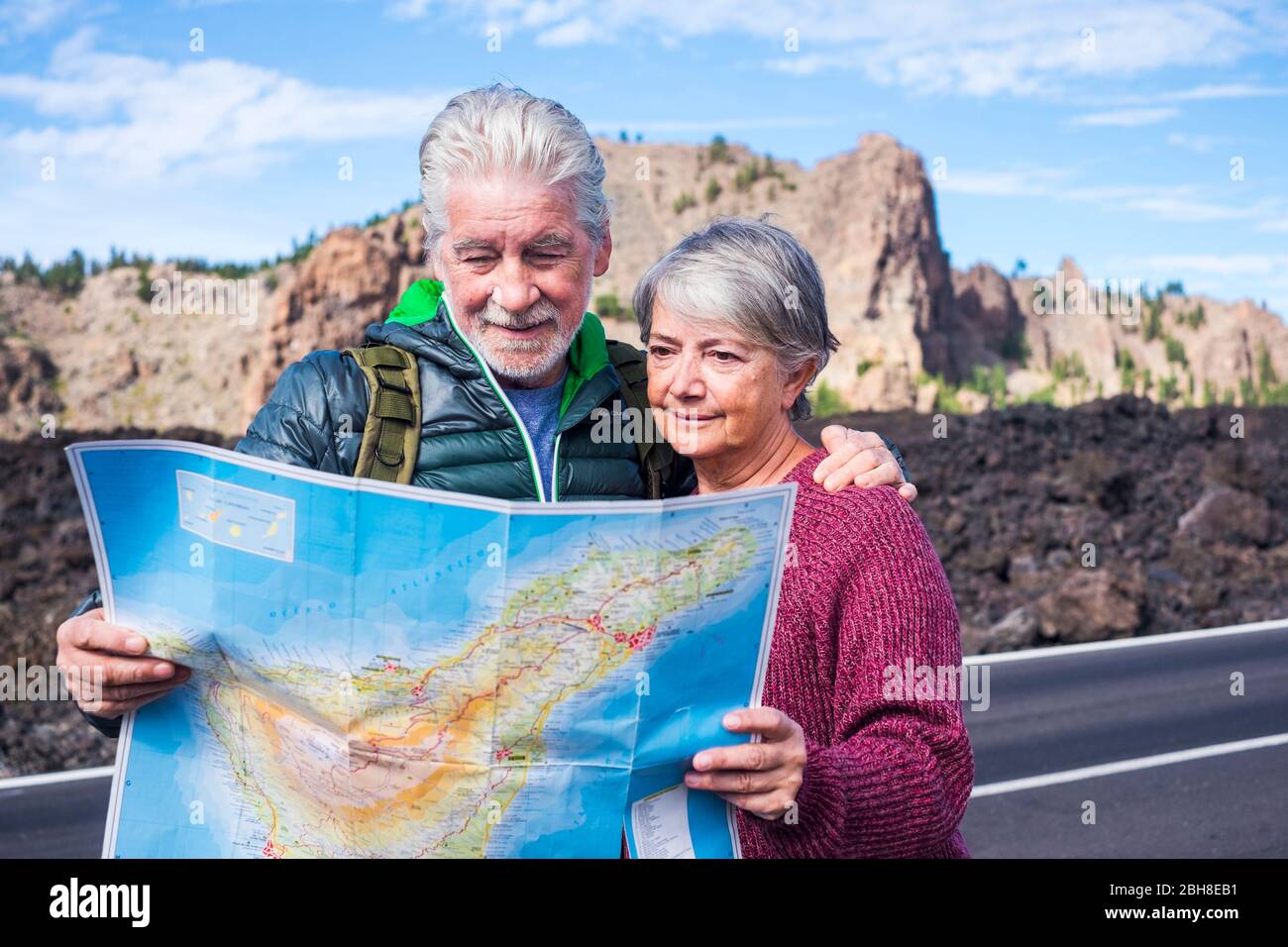 beautiful caucasian aged senior couple man and woman people traveling using old style paper map at the mountain - enjoy the lifestyle and retired life together with a backpack and needs of adventure and independence Stock Photo