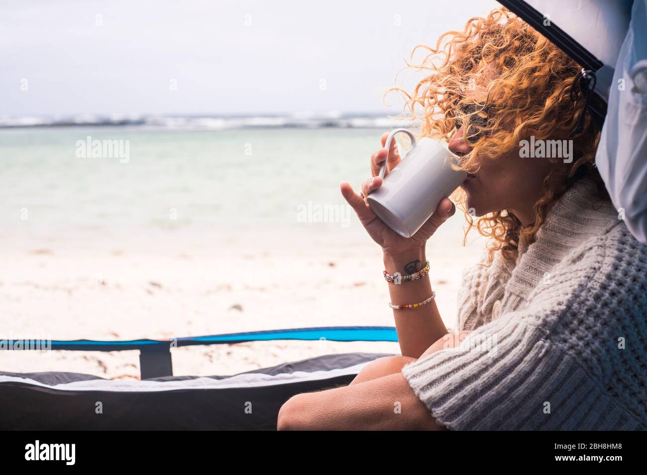 Beautiful middle age woman in free camping inside a tent on the ocean shore sandy beach enjoying alternative vacation - travel and adventure journey concept for caucasian modern lifestyle people Stock Photo