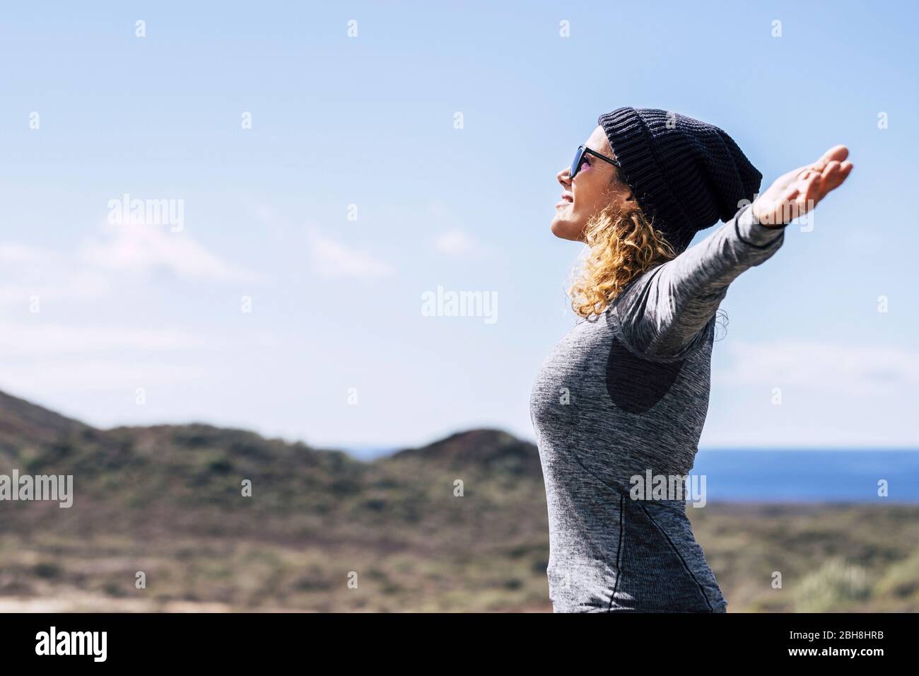 Happy full of joy beautiful caucasian woman with open arms enjoying the freedom and the wellnedd feeling the nature and the open air - hiker and trekking concept - blue ocean in background Stock Photo