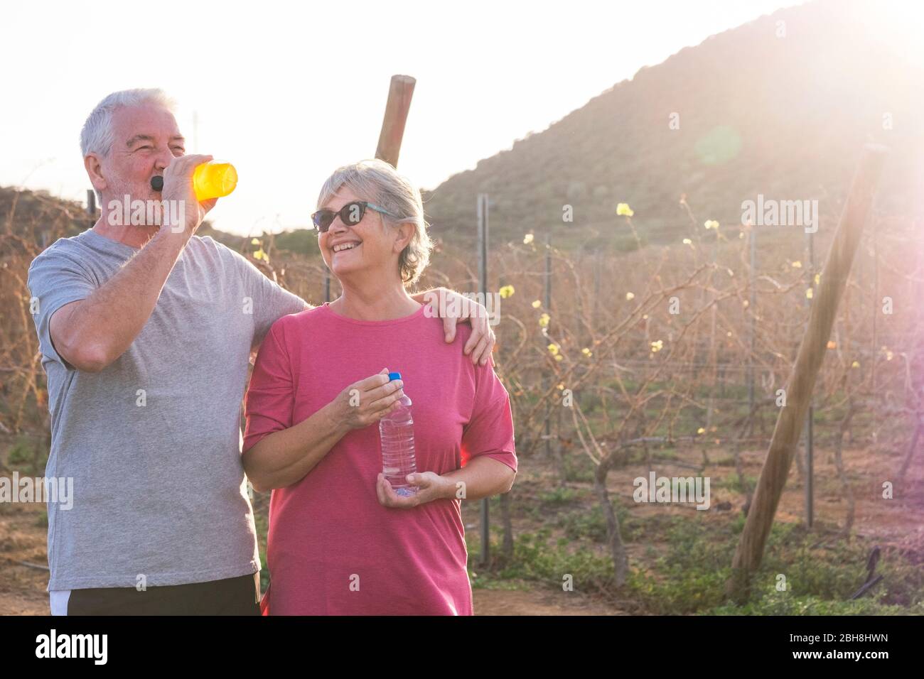 Man and woman caucasian people in outdoor leisure sport activity together - aged elderly concept - drinking energetic drink together - backlight in sunny day perfect for outside activities Stock Photo