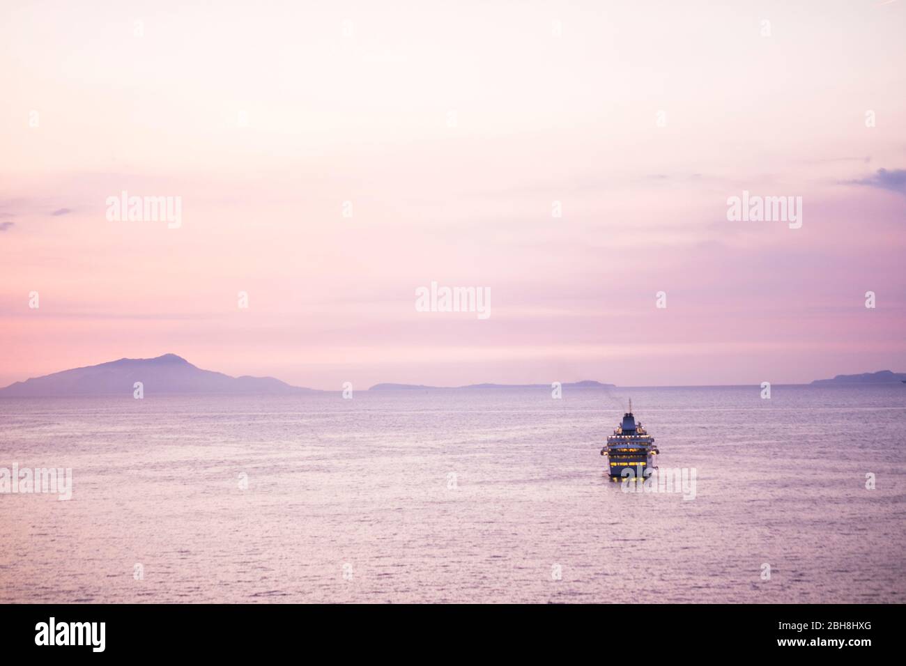 Travel and enjoy life concept with single boat in the middle of the sea with islands in background. Wanderlust with pink sunset sky coloured and people traveling away for the next adventure destination Stock Photo