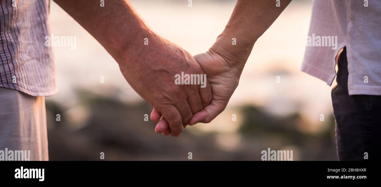 valentine's day love over time concept with hands of man and woman mature old people aged taking together each other with defocused background - romance and romantic picture for retired life Stock Photo