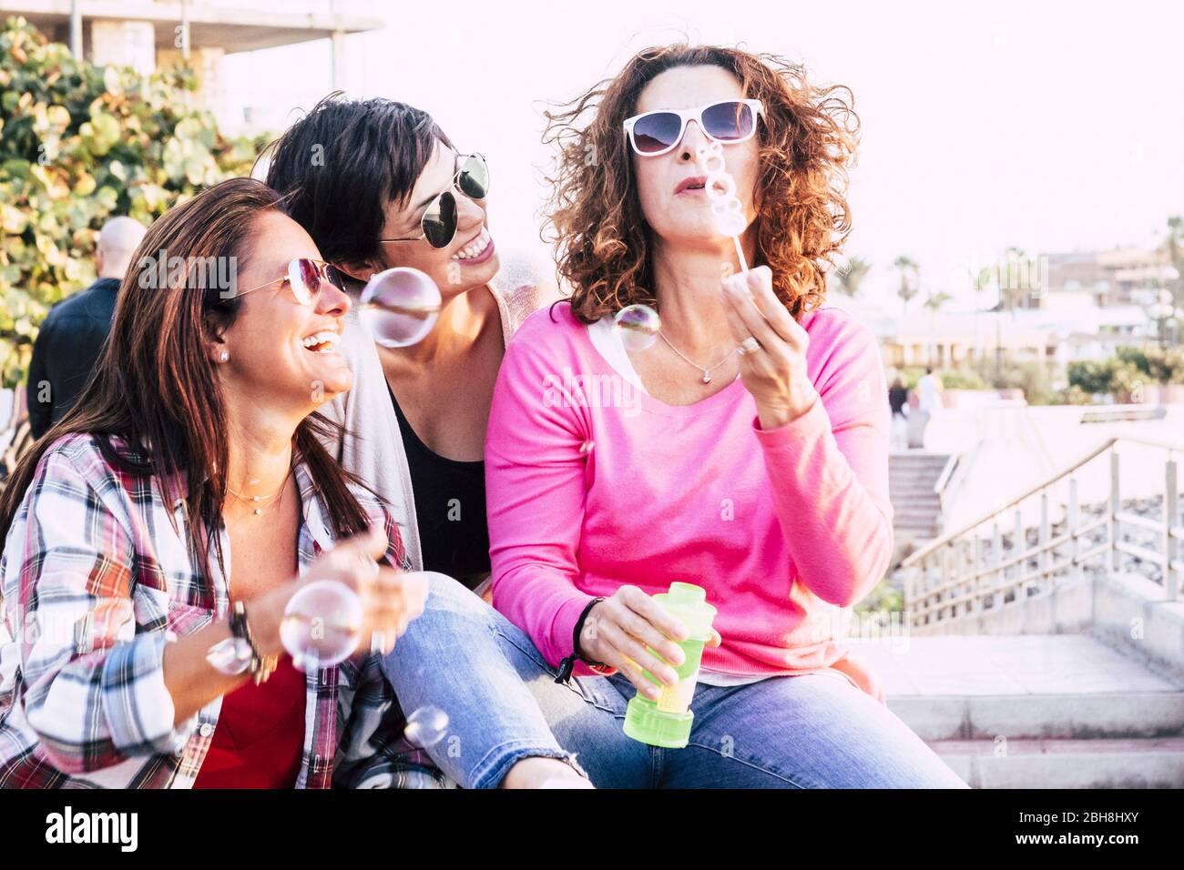 Playful real life concept with three cheerful smiling middle age women friends anejoying and laughing togehter playing with soap bubbles in outdoor leisure activity - playful and happiness concept for people Stock Photo