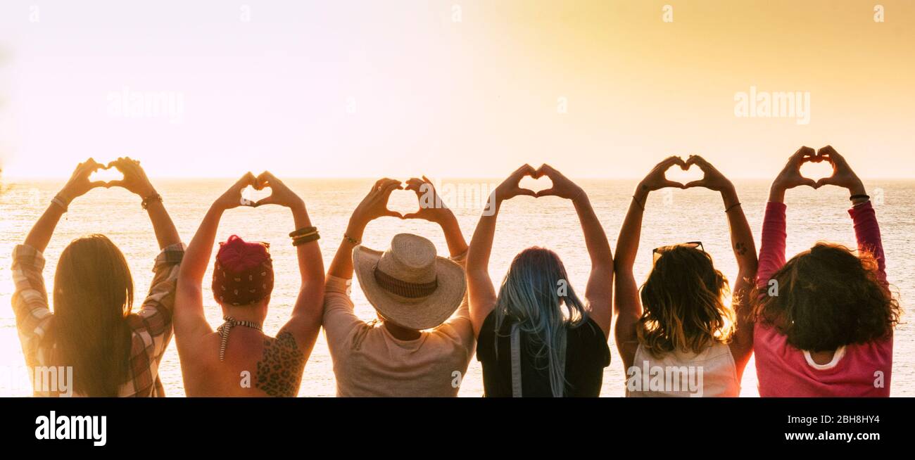 Group of diversity alternative young woman enjoying the sunset at the sea doing hearth symbol with hands - people enjoying friendly lifestyle - vacation in friendship concept for females Stock Photo