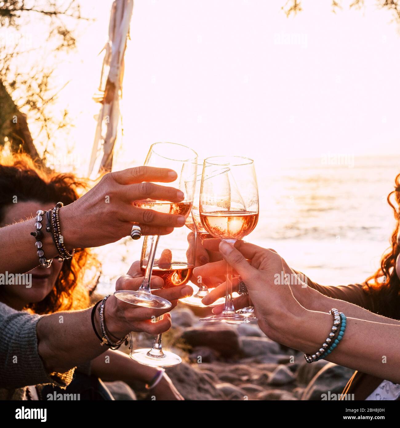 people drinking at party outdoor. group of friends white wine in hand toasting with glasses. close up on hands and drinks - beautiful scenic sunset and ocean in background for outdoor leisure activity in happiness Stock Photo