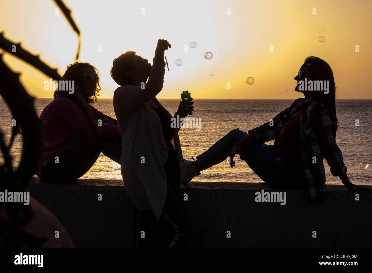 Friendship for women during the sunset - emotion and feeling with golden colors and three ladies in silhouette playing with bubbles soap - vacation and outdoor leisure activity concept Stock Photo