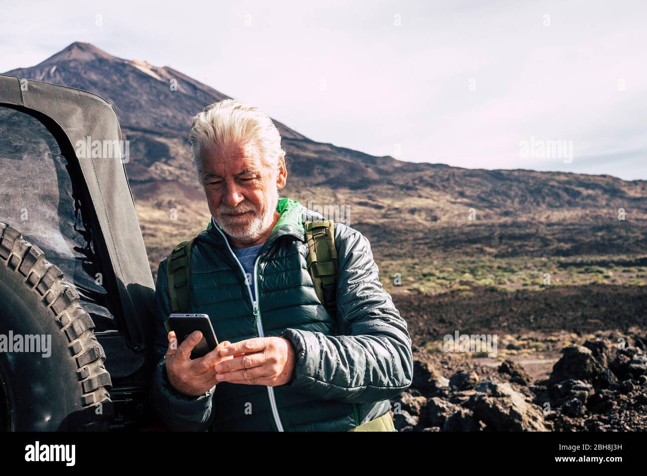 Caucasian old man use modern technology cellular phone at the mountain during trip vacation with off road car at the mountain - planning maps and roads enjoying the nature outdoor for alternative vacation with adventure Stock Photo