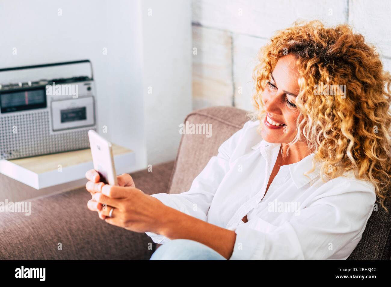 Cheerful attractive blonde curly hair young woman at home taking selfie ...