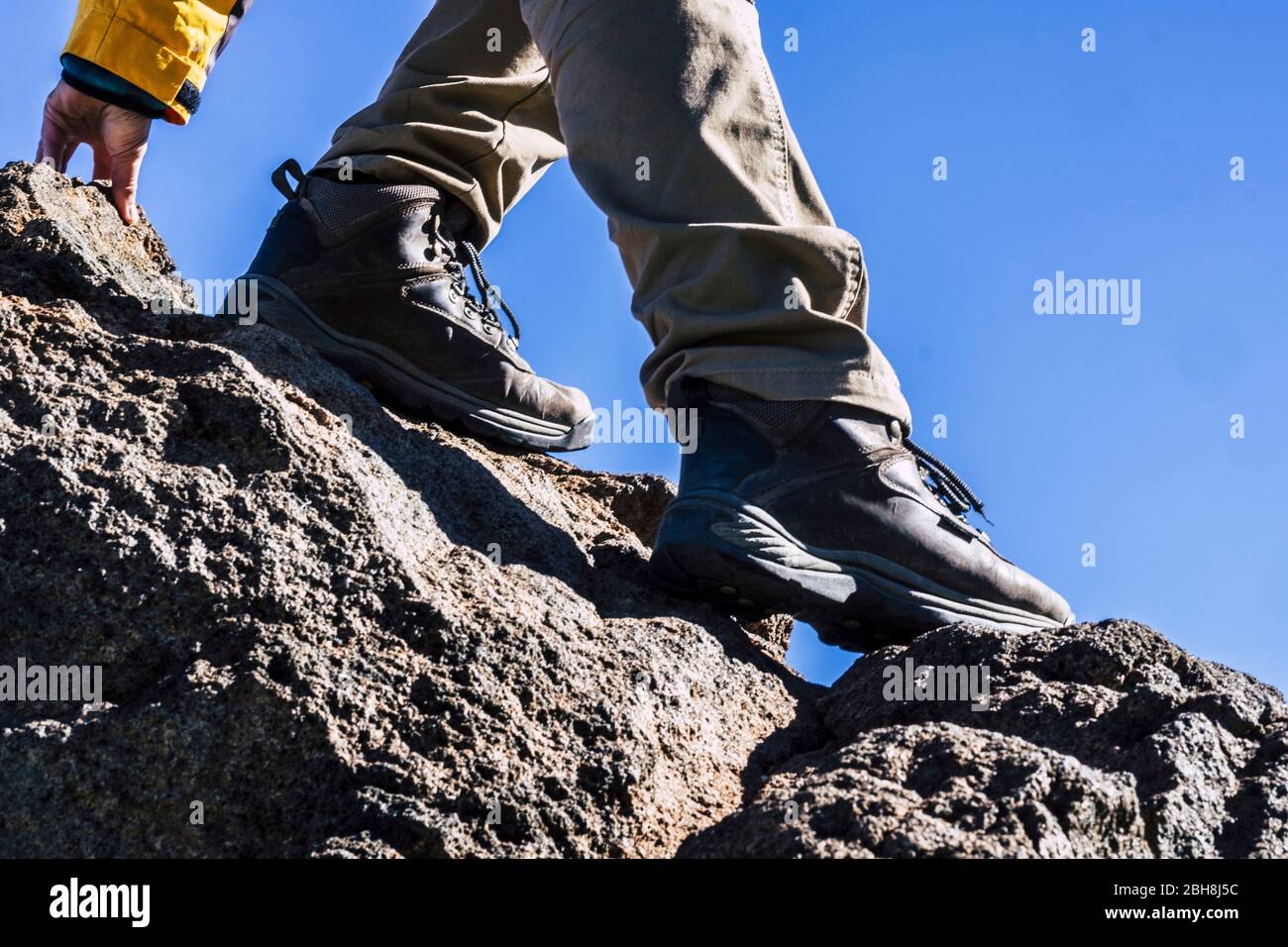 Close up of hiker legs and shoes rocking the mountain helping with one hand - concept of outdoor leisure activity and sport lifestyle - adventure and difficult enjoying the open air Stock Photo