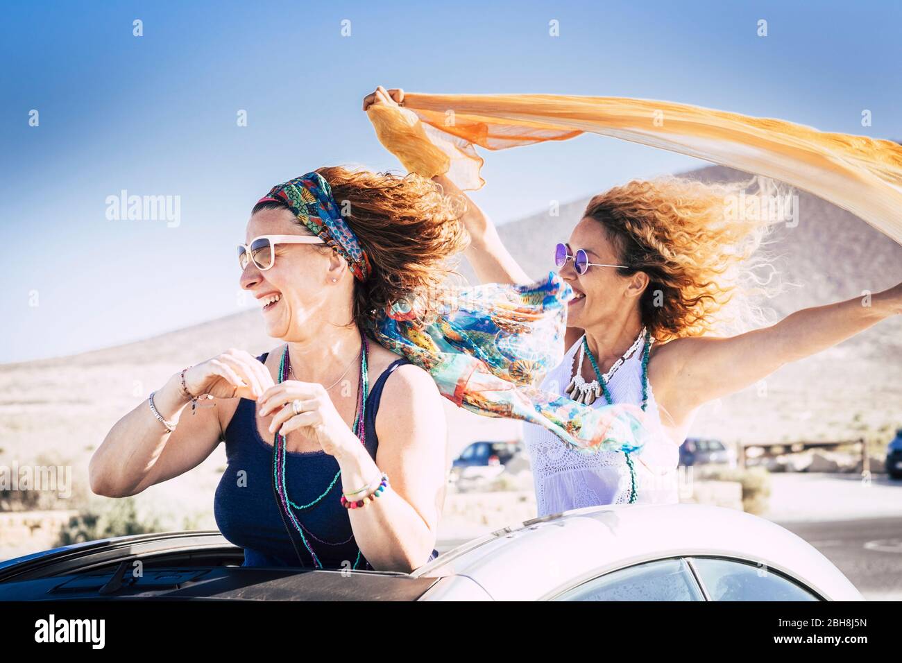 Couple of middle age caucasian woman cheerful and laughing enjoying the travel and the vacation with convertible car and playing with the wind for freedom lifestyle concept Stock Photo