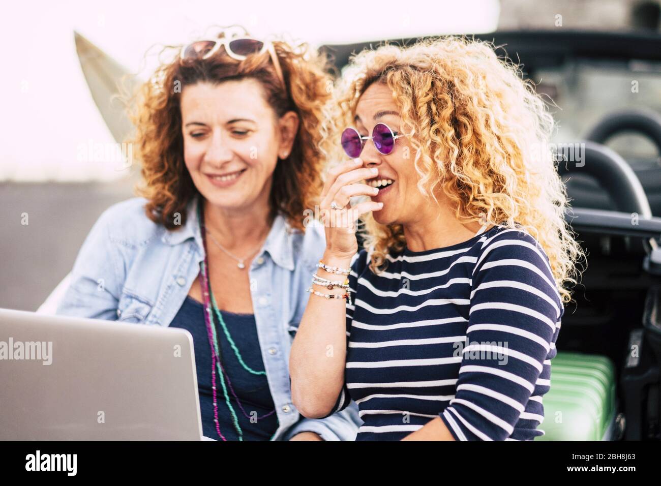 Couple of curly beautiful young women have fun laughing using a laptop outdoor - technoogy and people concept - funny things for pretty females - laugh and smile lifestyle Stock Photo