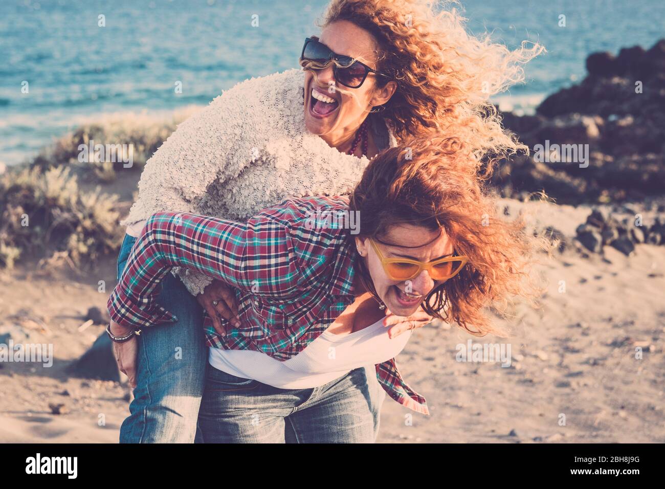 People laughing a lot and have fun together in friendship in outdoor leisure activity - couple of women gone crazy carrying eachother on the shoulder - no limit age to be playful and happy Stock Photo