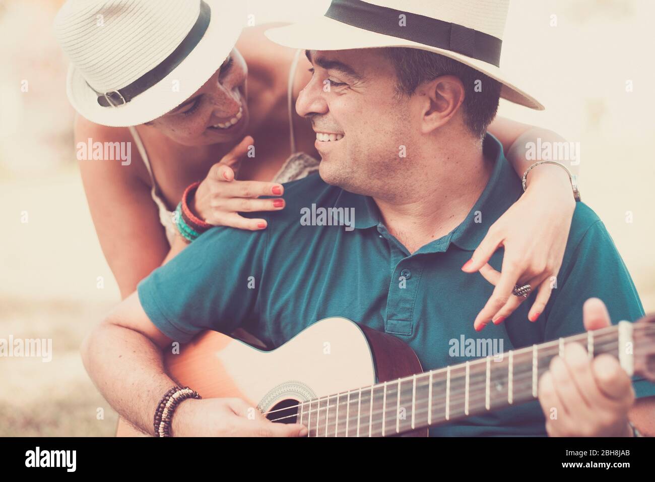 Romantic hug an colors with cheerful happy middle age people in love playing a guitar together looking and smiling - relationship for middle age adult caucasian couple - vintage filter tones Stock Photo