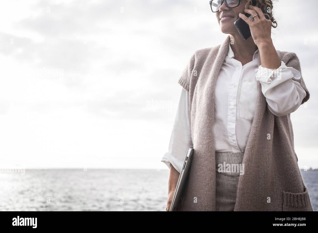 Caucasian middle age lady manager business woman work outdoor with ocean in background like free freelance with perfect lifestyle digitla nomad concept speak at the phone using internet connection worldwide everywhere Stock Photo