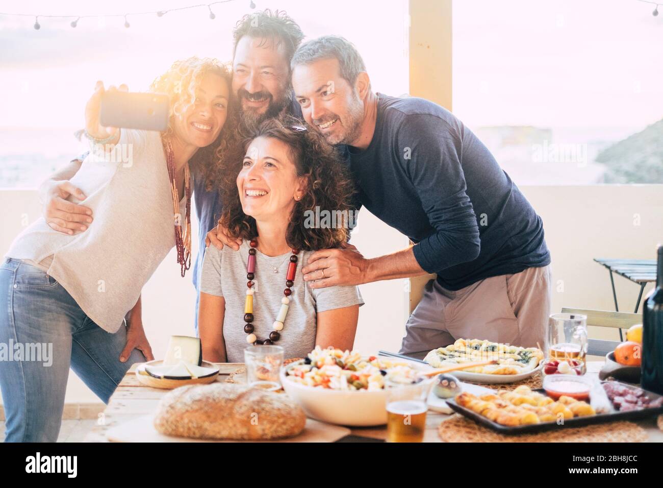 Group of friends have fun together during a lunch outdoor in the terrace at home and taking a modern selfie with smart phone to share on social media accounts for internet life - web addicted happy adult people Stock Photo