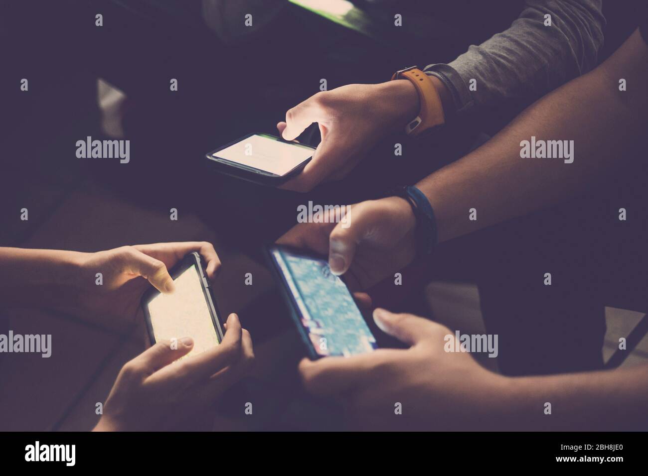 Three young caucasian teenager men play all together with mobile phone device to video games like clan or team - usual activity for millennial people at home - technology addicted people concept Stock Photo