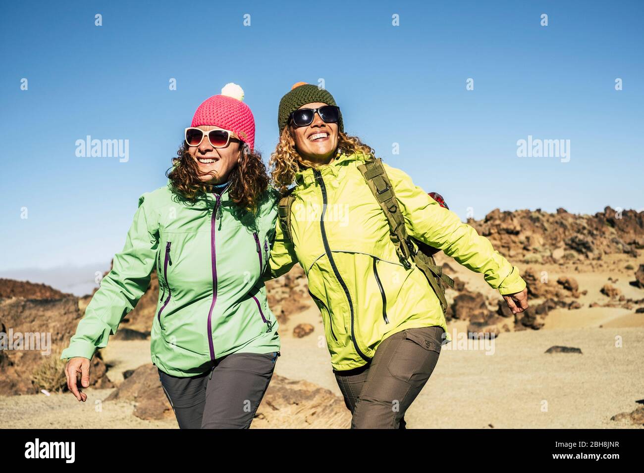 Happy cheerful couple of middle age women friends walking together at the mountain for alternative vacation - sunny day in outdoor leisure activity in the nature - happiness and joyful lifestyle for people Stock Photo