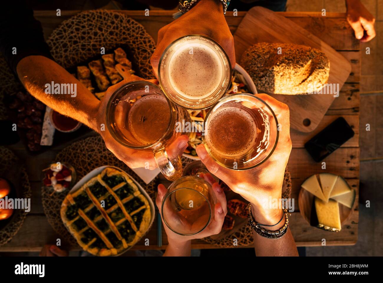 Top view of hands with beers cheering and having fun together - friends at dinner celebrating - wood table with a lot of food viewed from above - friendship and event party concept Stock Photo