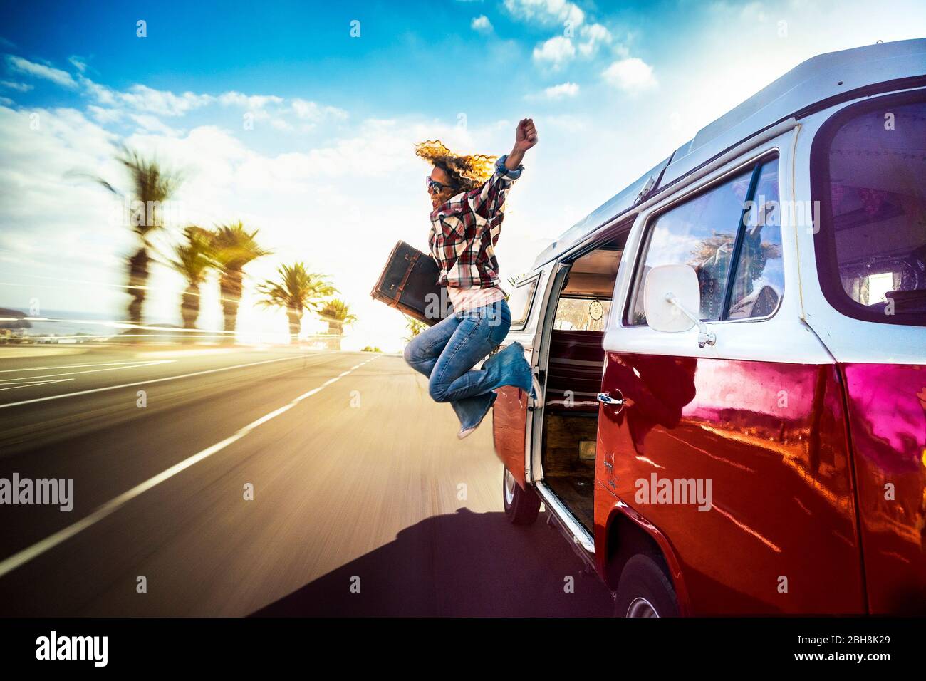 Happy middle age woman jumping outside a red vintage van while traveling fast on the road for the joy to start the vacation or adventure - wanderlust lifestyle for alternative holiday people Stock Photo
