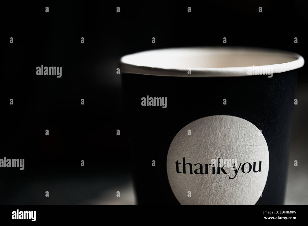 Fragment of black paper cup with the inscription thank you in black blurred background. Close up. Stock Photo