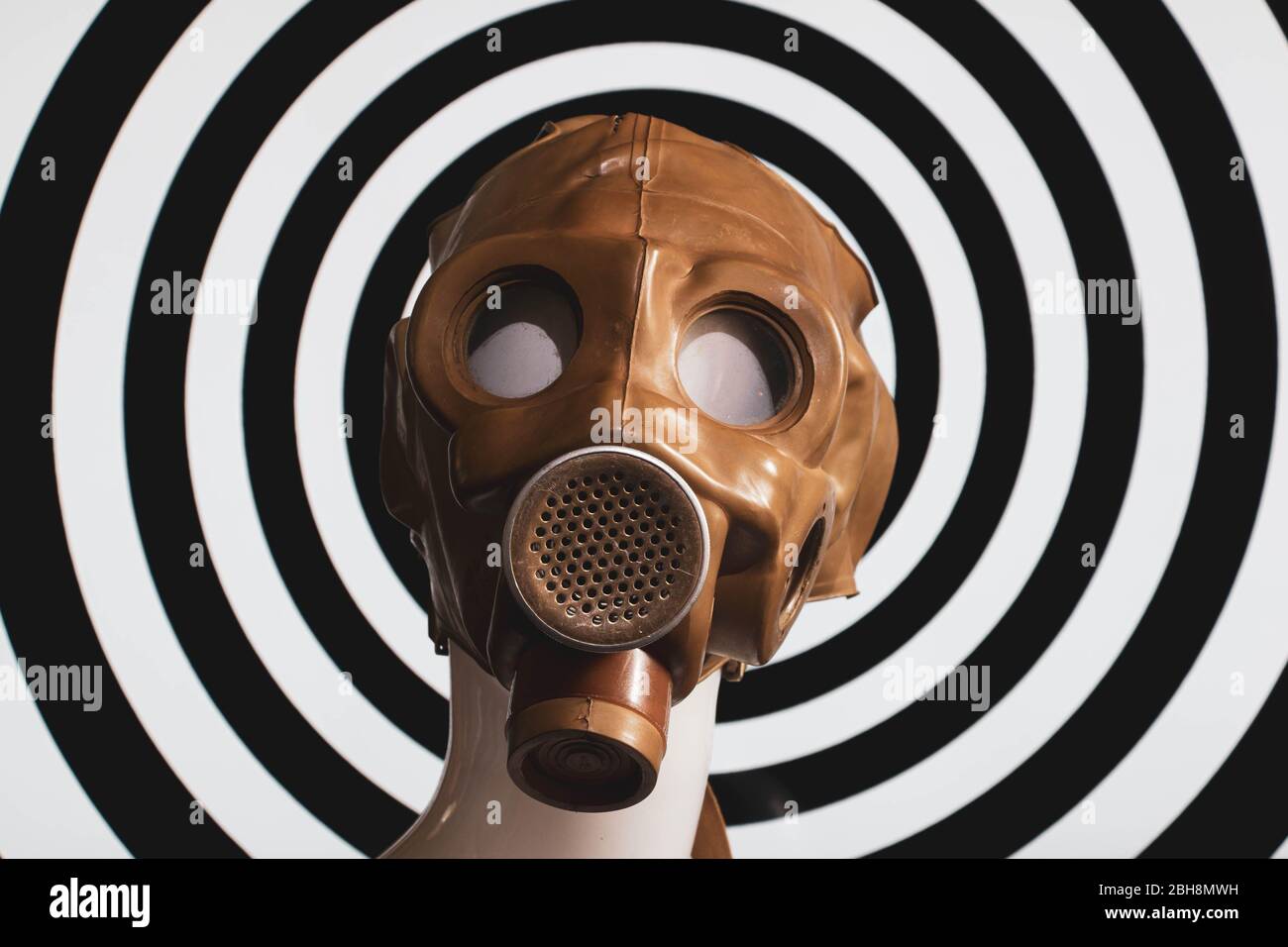 White mannequin wearing a vintage rubber gas mask against a black and white hypnotic spiral background. Stock Photo