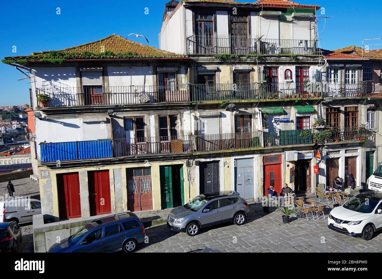 Picturesquely decaying row of old three & four storey residential buildings with multi-coloured front doors and iron balustraded balconies, in Porto Stock Photo
